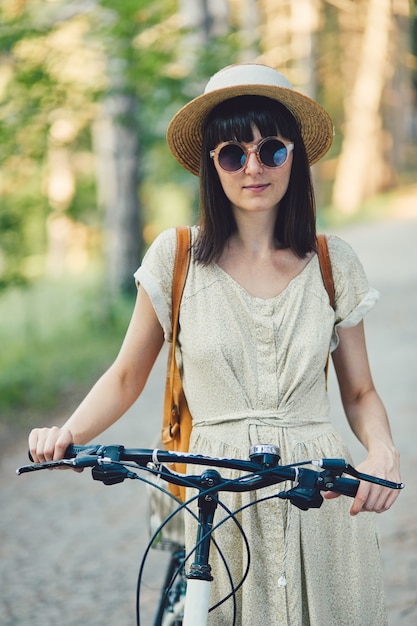 Ritratto all'aperto di giovane castana attraente in un cappello su una bicicletta.