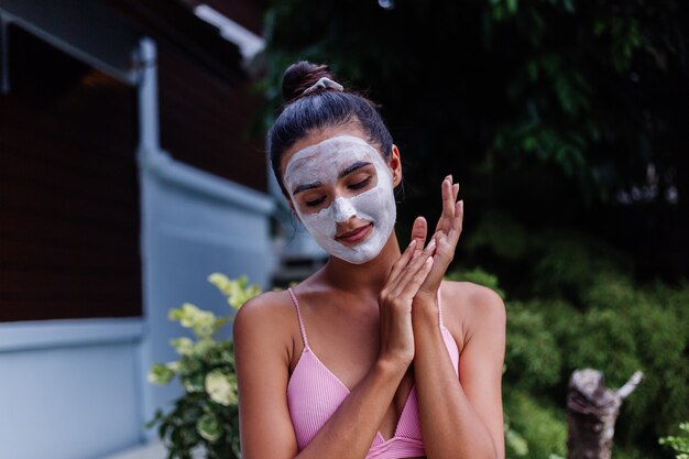 Ritratto all'aperto di pelle abbronzata calma donna abbastanza caucasica in bikini al centro benessere con maschera peeling bianca sul viso