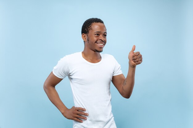 Ritratto alto vicino a mezzo busto di giovane modello maschio afro-americano in camicia bianca sull'azzurro