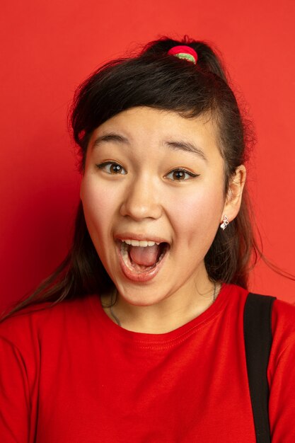 Ritratto alto vicino dell'adolescente asiatico isolato su sfondo rosso studio