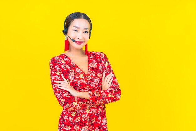 Ritratto bella giovane donna asiatica con auricolare per la cura del call center del cliente sulla parete gialla
