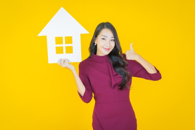 Ritratto bella giovane donna asiatica con casa o casa carta segno su yellow