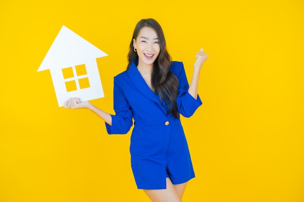 Ritratto bella giovane donna asiatica con casa o casa carta segno su yellow