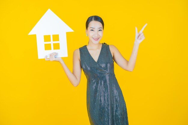 Ritratto bella giovane donna asiatica con casa o casa carta segno su yellow