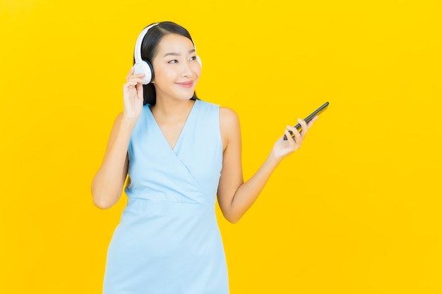 Ritratto bella giovane donna asiatica con cuffie e smart phone per ascoltare musica sulla parete gialla