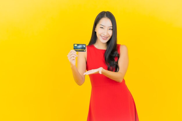 Ritratto bella giovane donna asiatica sorriso con carta di credito sulla parete gialla