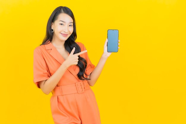 Ritratto bello giovane sorriso asiatico della donna con il telefono cellulare astuto su colore giallo