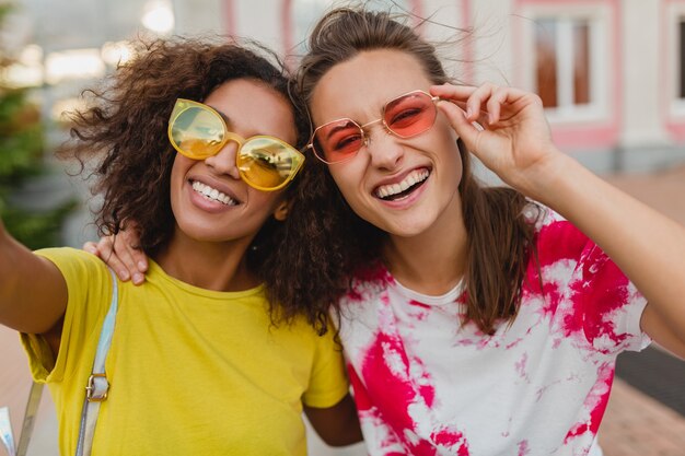 Ritratto colorato di amici di ragazze giovani felici sorridente seduto in strada prendendo foto selfie sul telefono cellulare, donne che si divertono insieme