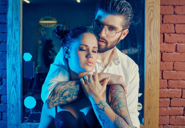 Ritratto colorato di bella coppia: uomo brutale in abito elegante e ragazza con un tatuaggio che indossa lingerie nel negozio di barbiere