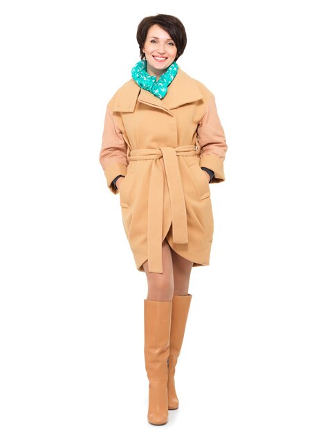 Ritratto completo di donna felice in cappotto beige autunno e stivale in pelle con sciarpa verde in piedi isolato su bianco