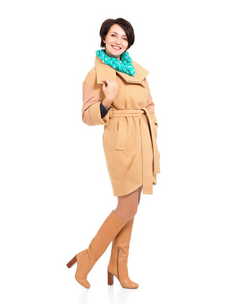 Ritratto completo di donna felice in cappotto beige autunno e stivale in pelle con sciarpa verde in piedi isolato su bianco