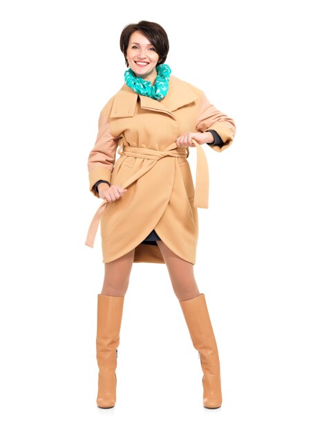 Ritratto completo di donna felice in cappotto beige autunno e stivale in pelle con sciarpa verde in piedi isolato su bianco