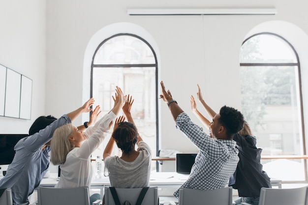 Ritratto dal retro di studenti stanchi che si allungano dopo un lungo lavoro. Foto dell'interno di impiegati che scherzano durante la riunione nella sala conferenze con grandi finestre.