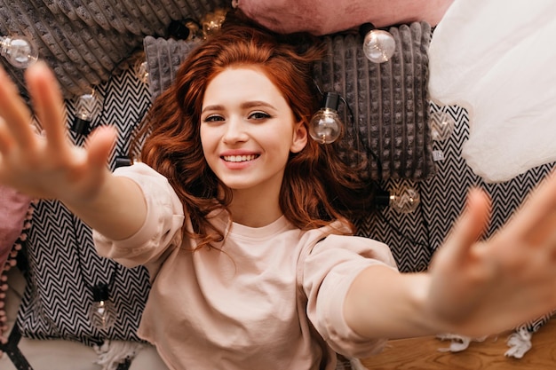 Ritratto dall'alto di una ragazza bianca riccia che si prepara per le vacanze Foto interna di una donna spensierata allo zenzero che posa con un sorriso sincero