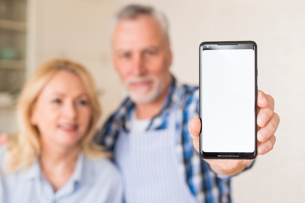 Ritratto Defocused di un telefono cellulare della tenuta delle coppie senior con la visualizzazione di schermo bianca