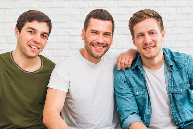 Ritratto degli amici maschii sorridenti che esaminano macchina fotografica contro il muro di mattoni bianco