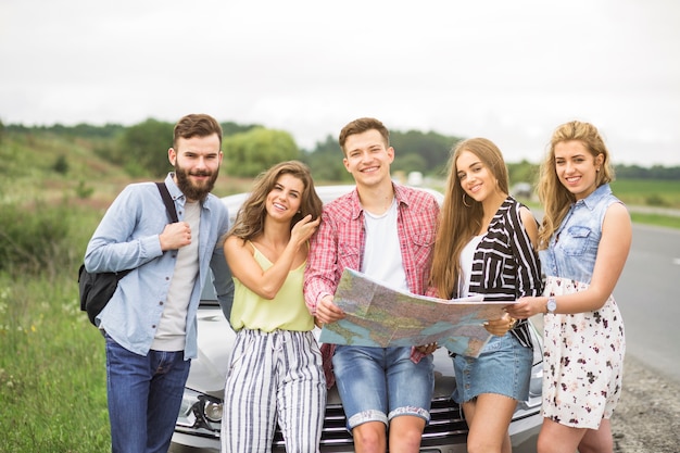 Ritratto degli amici turistici che tengono mappa che sta davanti all&#39;automobile all&#39;aperto