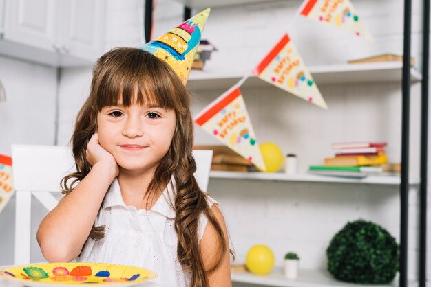 Ritratto del cappello di partito da portare sorridente della ragazza sveglia di compleanno