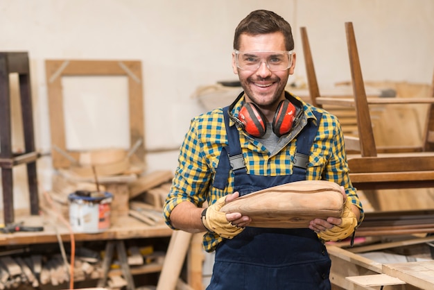 Ritratto del carpentiere maschio sorridente che tiene modello di legno incompleto