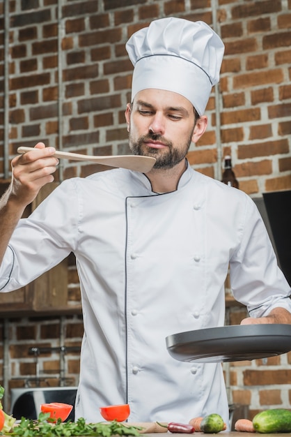 Ritratto del cuoco unico maschio che sta in cucina che assaggia alimento