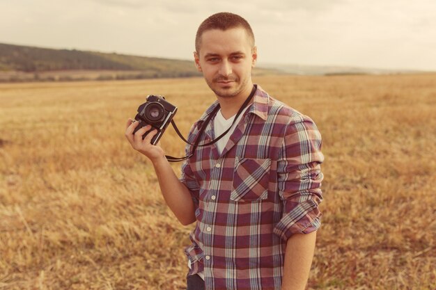 Ritratto del fotografo maschio attraente all'aperto al tramonto. Giovane con una macchina fotografica in mano