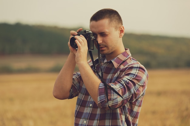 Ritratto del fotografo maschio attraente all'aperto al tramonto. Giovane con una macchina fotografica in mano