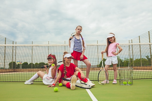 Ritratto del gruppo di ragazze come tennis che tengono la racchetta di tennis contro l'erba verde della corte all'aperto