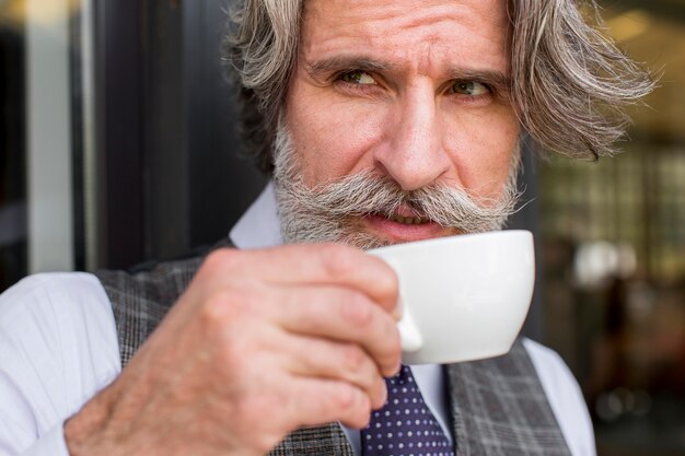 Ritratto del maschio elegante che gode della tazza di caffè