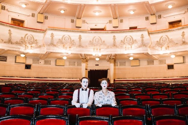 Ritratto del mimo maschio e femminile che si siede sulla sedia rossa nell&#39;auditorium