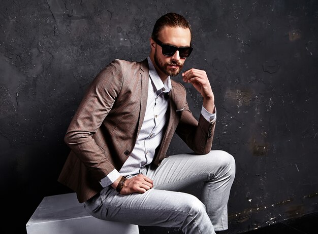 ritratto del modello di uomo d'affari alla moda hipster alla moda bello vestito in elegante abito marrone seduto vicino al buio