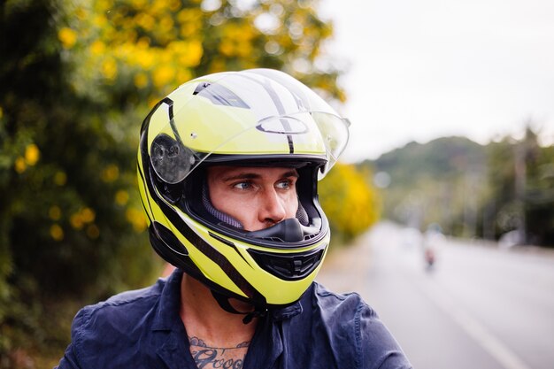 Ritratto del motociclista maschio in casco giallo sulla moto sul lato della strada trafficata in Thailandia