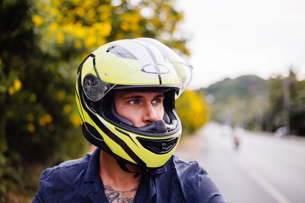 Ritratto del motociclista maschio in casco giallo sulla moto sul lato della strada trafficata in Thailandia