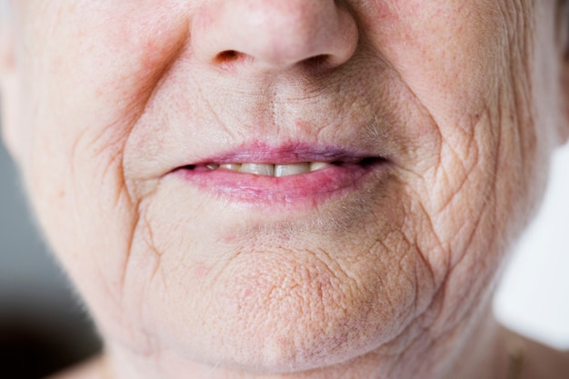 Ritratto del primo piano bianco della donna anziana sulle labbra sorridenti