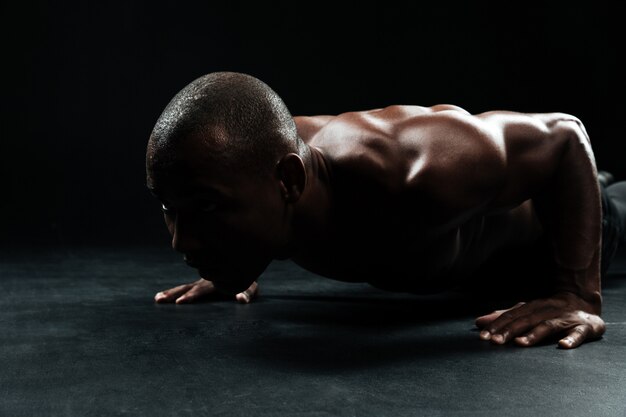 Ritratto del primo piano dell'uomo afroamericano di sport, con il bello ente muscolare che fa esercizio di piegamento sulle braccia sul pavimento