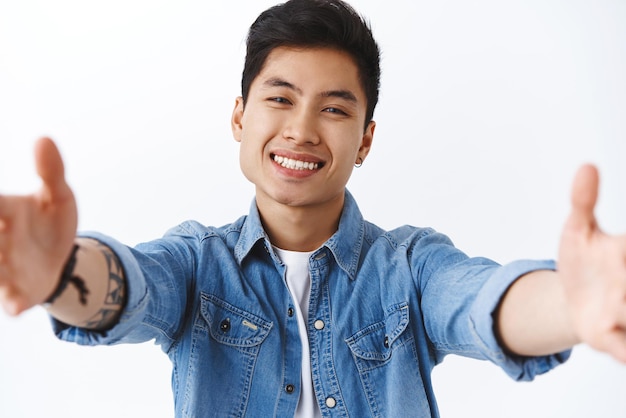 Ritratto del primo piano dell'uomo asiatico adorabile amichevole che raggiunge le mani in avanti per la macchina fotografica della tenuta dell'abbraccio facendo uso della compressa digitale alla famiglia di videochiamata mentre restando a casa sorridente allegro fondo bianco