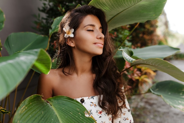 Ritratto del primo piano della donna pacificata con il fiore nei capelli ondulati scuri