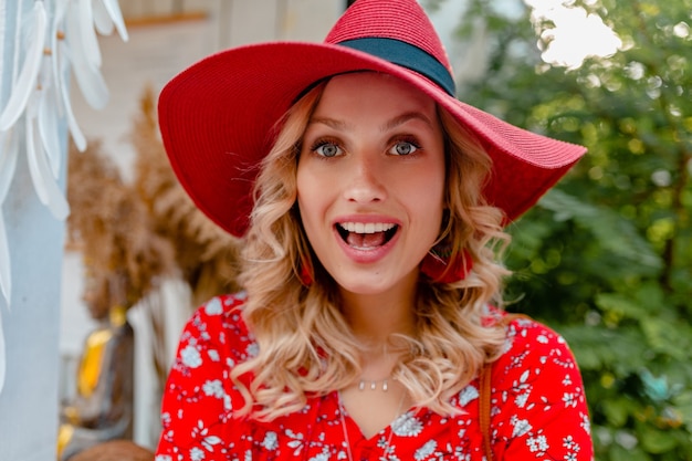 Ritratto del primo piano della donna sorridente bionda alla moda attraente in cappello rosso della paglia e vestito di modo di estate della camicetta con il sorriso