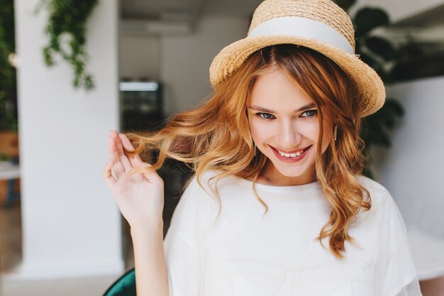 Ritratto del primo piano della ragazza felice dagli occhi azzurri che gioca con i capelli ricci