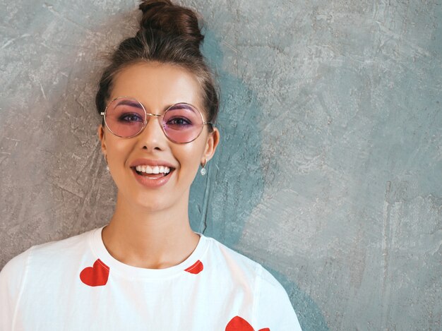 Ritratto del primo piano di giovane bello sguardo sorridente della donna. Ragazza alla moda in abito bianco estivo casual e occhiali da sole.