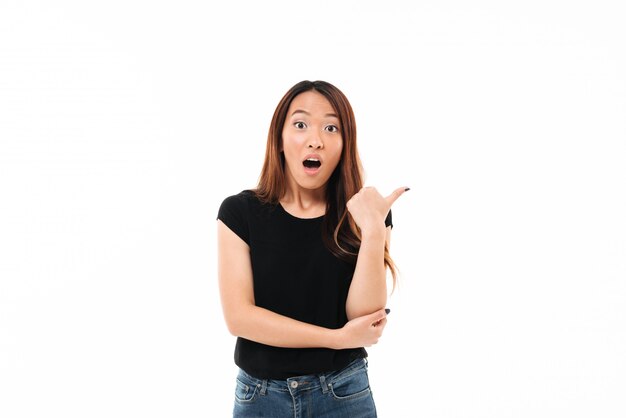 Ritratto del primo piano di giovane donna abbastanza asiatica colpita che mostra pollice sul gesto, esaminante macchina fotografica