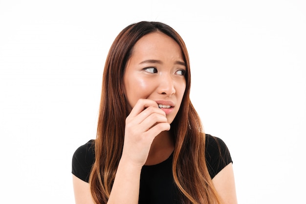 Ritratto del primo piano di giovane donna asiatica spaventata che sta con il dito nella sua bocca, lookin da parte
