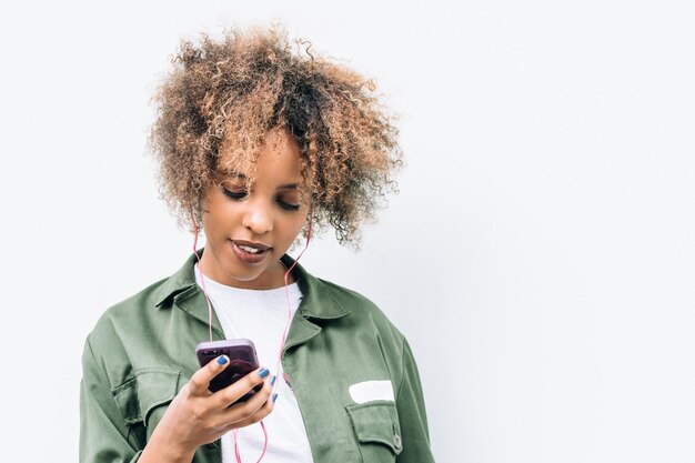 Ritratto del primo piano di giovane donna moderna che ascolta la musica sul telefono cellulare fuori sulla via della città