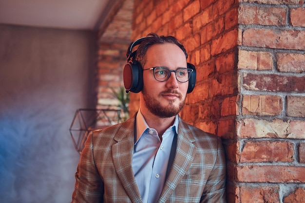 Ritratto del primo piano di un uomo alla moda in un vestito di flanella e occhiali che ascolta musica.