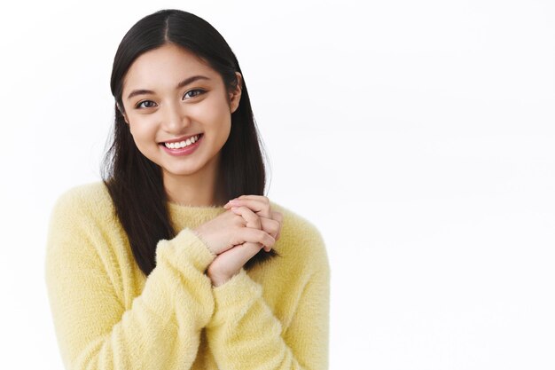 Ritratto del primo piano ragazza asiatica carina femminile in maglione giallo, premere le mani insieme e sorridere adorabile, promuovere cosmetici coreani o asiatici