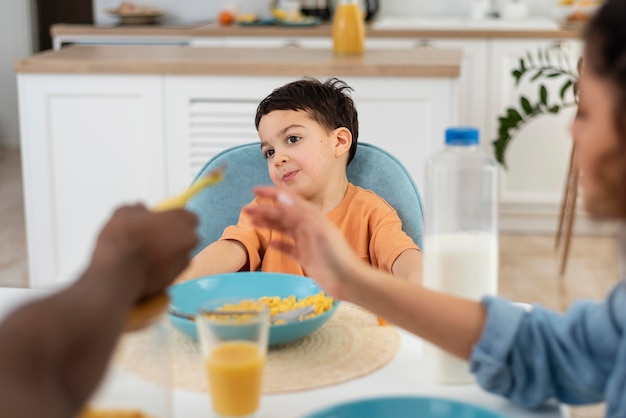 Ritratto del ragazzino sveglio che mangia prima colazione con i genitori