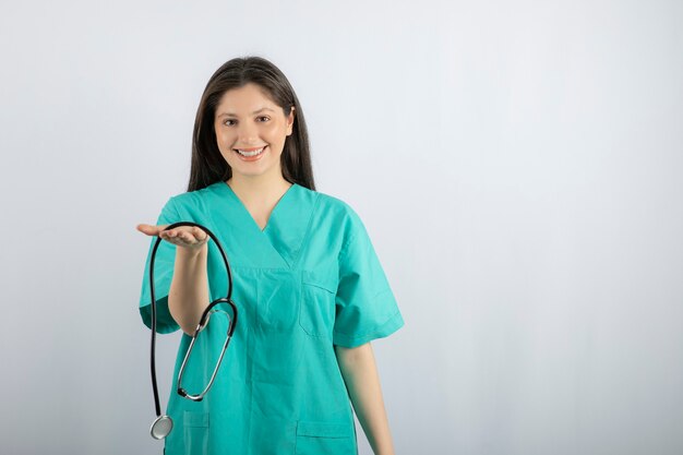 Ritratto dell'infermiera femminile che mostra lo stetoscopio su bianco.