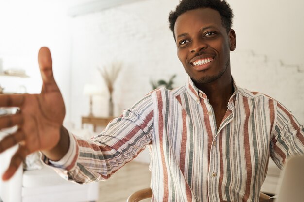 Ritratto dell'interno del giovane africano sicuro bello in camicia a strisce che ha espressione facciale amichevole