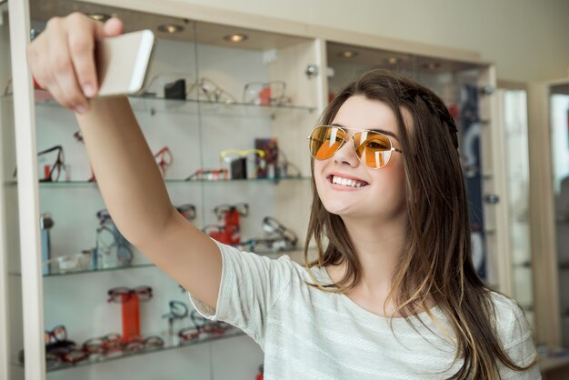 Ritratto dell'interno di bella giovane donna nel negozio di ottica, acquisto di nuovi occhiali da sole per proteggere gli occhi dal sole