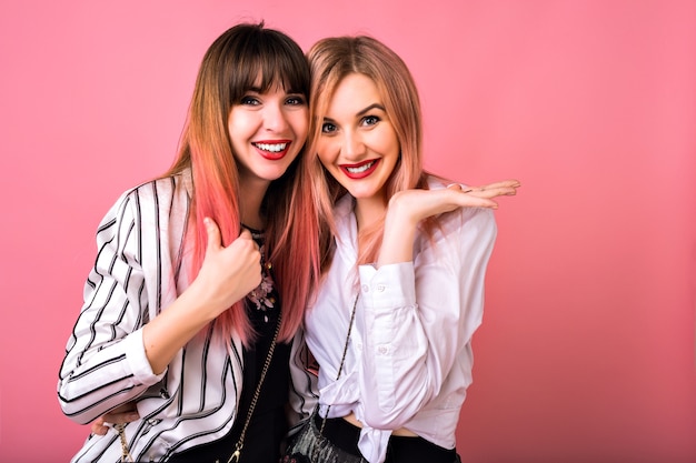 Ritratto dell'interno di due donne sorelle felici migliori amici, che indossano abiti alla moda in bianco e nero e capelli rosa, abbracci e sorridenti, emozioni uscite, stile hipster