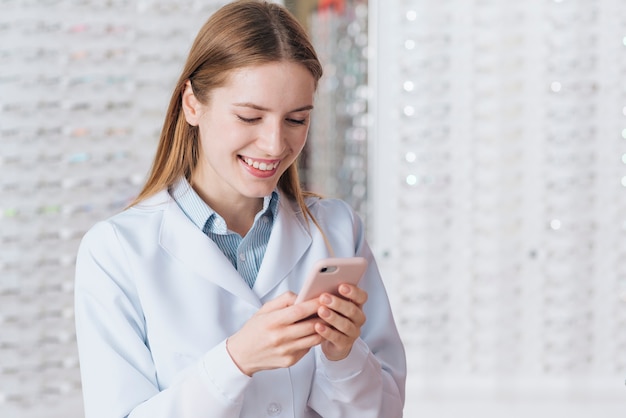 Ritratto dell&#39;optometrista femminile amichevole che per mezzo dello smartphone